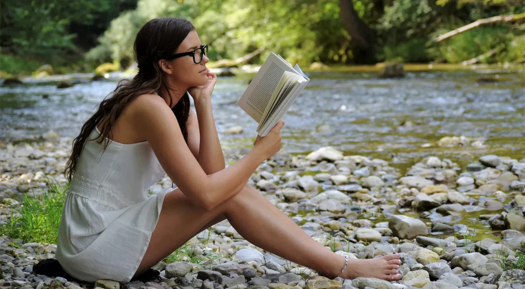 河原で身軽な服装で読書をする女性