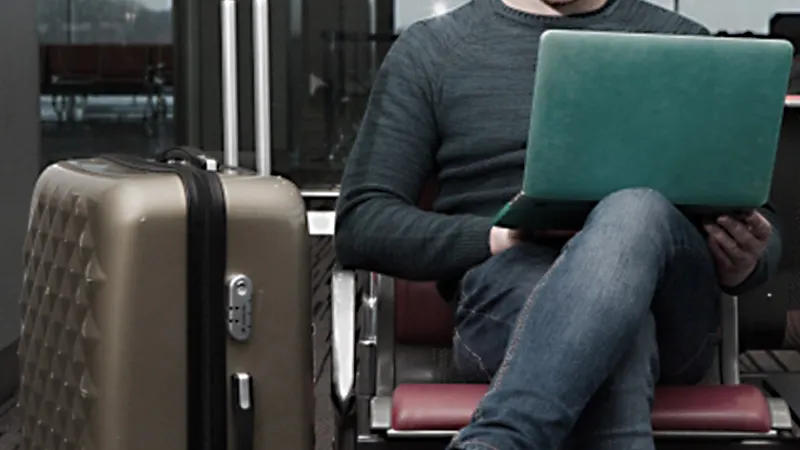 椅子に座ってノートパソコンを使う旅行者